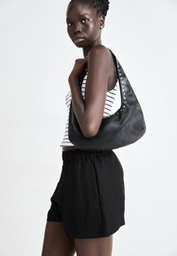 Sac en cuir noir avec des clous en métal le long de la bandoulière, porté avec un débardeur rayé et un short noir ample.