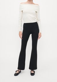 Top blanco acanalado sin hombros combinado con pantalones negros de campana y bailarinas negras con un lazo decorativo y detalles de tachuelas.