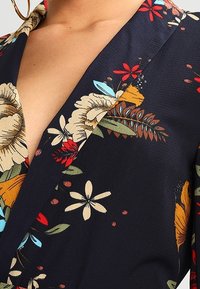 Blusa floreale in tessuto blu navy scuro con fiori vivaci in rosso, giallo e blu. Colletto con intaglio e tessuto leggero.