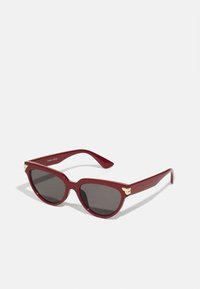 Gafas de sol rojas con un acabado brillante, forma de ojo de gato, acentos dorados en las patillas y lentes oscuros. Diseñadas por Anna Field.