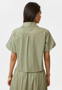 Kortarmige, lichtgroene blouse met een relaxte pasvorm, knoopsluiting bij de kraag, geplooide achterkant en gladde, lichtgewicht stof.