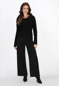 Pulover negru din tricot cu model de cable, cu un guler lat, asociat cu pantaloni largi negri, cu talie înaltă. Ținuta are o finisare texturată.
