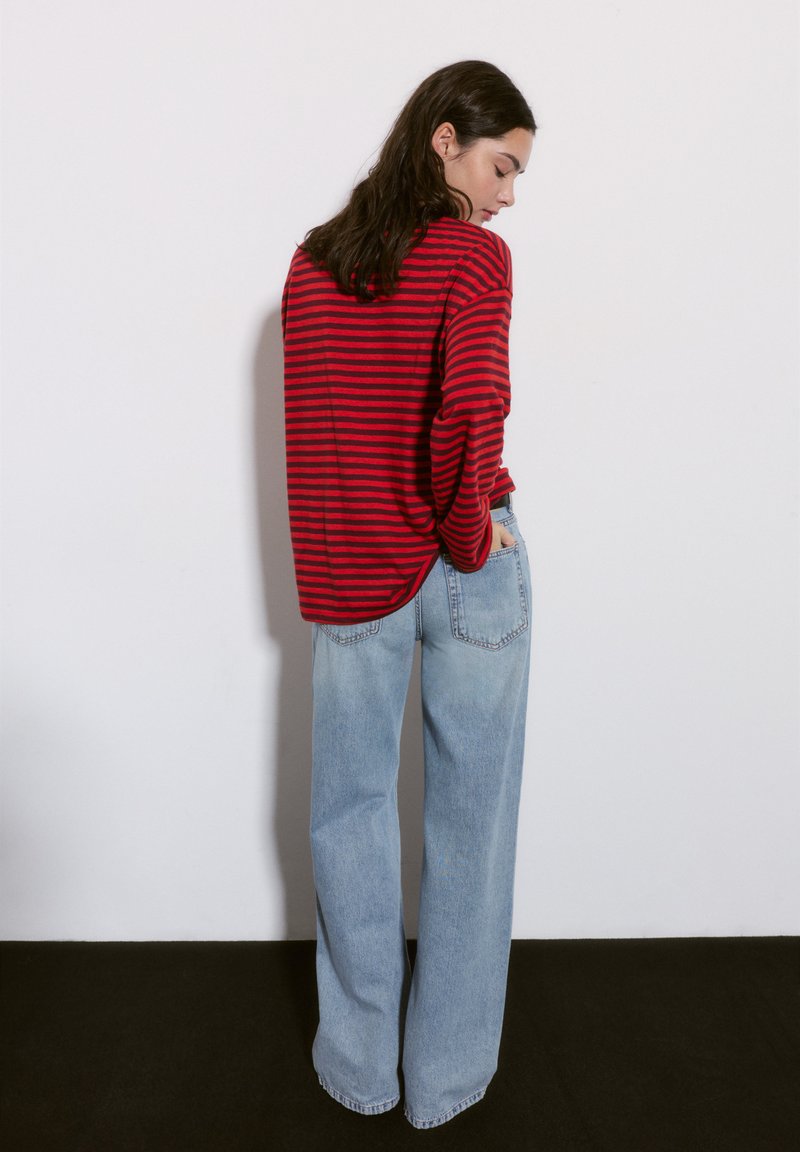 Czerwono-granatowy paskowany longsleeve sparowany z jasnoniebieskimi spodniami wide-leg o wysokim stanie; swobodny fason z zaokrąglonym dołem i przednimi kieszeniami.