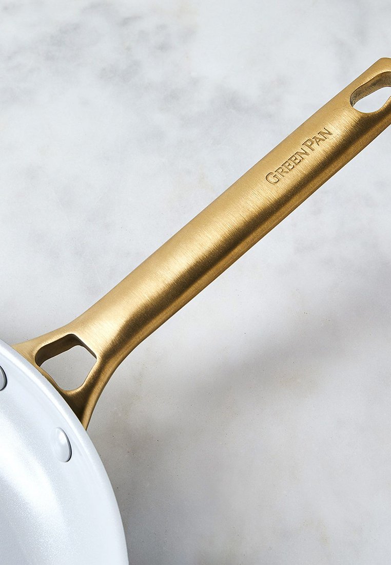 Sartén blanca con un mango texturizado dorado, que cuenta con un agujero para colgar. El mango tiene "GREENPAN" grabado en él.