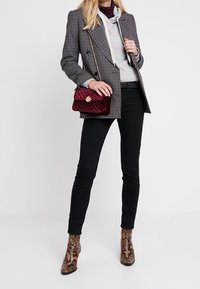 Blazer cruzado de cuadros gris sobre una sudadera con capucha gris, vaqueros pitillo negros y botines marrones con estampado de serpiente. Bolso acolchado color burdeos.