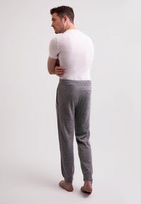 Graue Sweatpants mit lockerer Passform, elastischem Bund und einer Gesäßtasche. Kombiniert mit einem eng anliegenden weißen T-Shirt. Barfußmodell von hinten betrachtet.