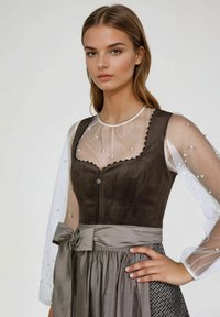 Bruin suede lijfje met golvende randen, zilveren rits, doorzichtige witte mouwen versierd met parels en een grijze rok met patroondetail.