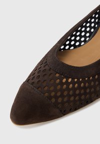 Καφέ σουέντ φλατ παπούτσια με διάτρητο σχέδιο, μυτερή μυτούλα και λεία εσωτερική επένδυση. Το παπούτσι έχει κομμένο στυλ και υφή στο πάνω μέρος.