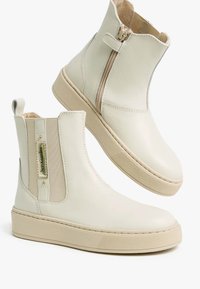 Cremfarbene Lederstiefeletten mit einem seitlichen Reißverschluss, elastischen Einsätzen, strukturierten Gummisohlen und einem kleinen Logo-Akzent. Glatte Oberfläche, minimalistisches Design.