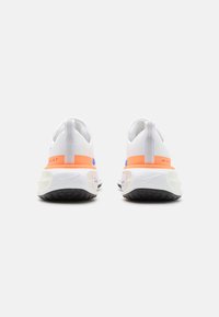 Witte sportschoenen met oranje en paarse accenten, bovenwerk van getextureerde stof, onderscheidende hielvorm en het kenmerkende Nike-logo op de zool.