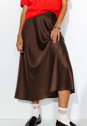 Jupe midi en satin brun avec une texture lisse et un design fluide, associée à des chaussettes blanches portant un texte rouge et des mocassins noirs.