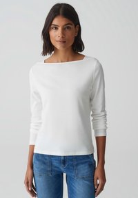 Witte lange mouw top met een vierkante halslijn, gemaakt van gladde stof. In combinatie met blauwe spijkerbroek met voorzakken en een relaxed fit.
