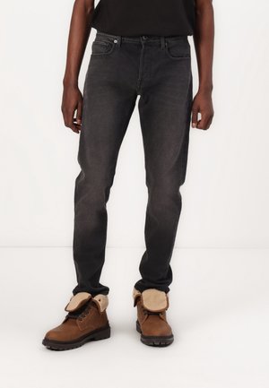 Jeans ajustados de color gris oscuro con un diseño clásico de cinco bolsillos, combinados con botas marrones que presentan un collar de pelaje sintético y una suela texturizada.