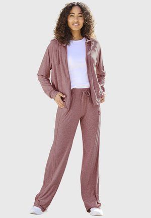 Woman smiling, wearing a dusty rose hoodie and matching drawstring pants with white sneakers and a white t-shirt.