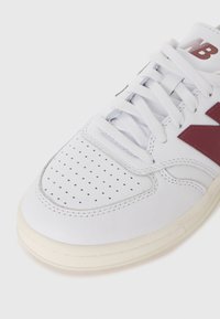 Hvite lærersneakers med maroon aksenter, perforert tåområde, flate hvite snøringer og teksturert gummisåle. Rund tå og sømdetaljer.