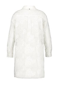 Longue chemise blanche en dentelle florale avec manches longues et poignets boutonnés vue de dos.
