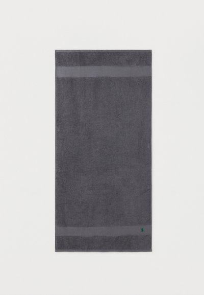 Σκούρο γκρι ορθογώνια πετσέτα μπάνιου με δύο οριζόντιες ταινίες κοντά στις άκρες και ένα μικρό πράσινο κεντημένο λογότυπο στην κάτω δεξιά γωνία.