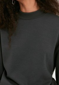 Sudadera gris oscuro con un cuello acanalado alto, textura suave y corte relajado, con costuras visibles y un diseño minimalista.