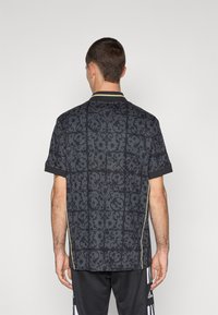 Fekete mintás ing, texturált mintával, rövid ujjú, kontrasztos gallérral, sárga kiemelésekkel. Könnyű anyagból készült.