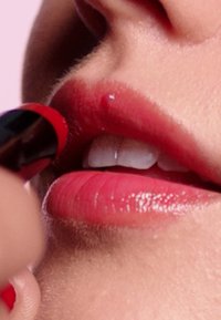 Czerwona szminka nakładana na pełne, lśniące usta. Usta mają delikatny różowy odcień, gładką teksturę i naturalny blask.