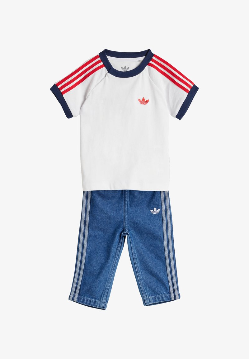 Vaikiška Adidas apranga, susidedanti iš baltos marškinėlių su raudonomis juostelėmis ant rankovių ir mažu logotipu, derinama su mėlynais džinsiniais kelnėmis su šoninėmis juostelėmis.