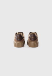 Sneakers in suede e pelle marroni con piattaforma, foderati con una pelliccia beige testurizzata. Presentano una suola a coste color tan e testo in oro in rilievo sul tallone.