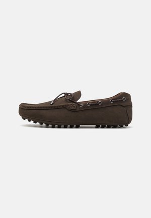 Mocassin pour homme en daim marron foncé avec coutures mocassin, détail de lacet sur le dessus et autour du talon, et semelle cloutée en caoutchouc, visible de profil.