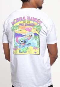 White t-shirt featuring a colorful graphic of a cartoon character and beach scene, with text reading "Aloha Hawaii! Come Visit the Islands."