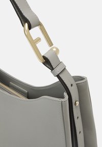 Szara skórzana torebka o gładkiej fakturze, z ozdobą z złotego metalu oraz regulowanym paskiem w minimalistycznym stylu.