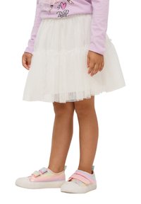 Gonna in tulle bianco con strati di rouches e luccichii, abbinata a sneaker in tonalità pastello arcobaleno con strap a velcro e suola bianca.