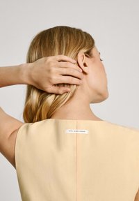 Svijetložuta haljina s okruglim izrezom i glatkom teksturom. Na stražnjoj strani se nalazi oznaka s natpisom "PEPE JEANS LONDON".