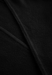 Détail de tissu noir présentant une surface douce et texturée avec des sections qui se superposent, dotée d'un léger éclat et de bords lisses.