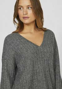 Suéter gris de punto con cuello en V, textura acanalada y corte holgado. Las mangas son anchas y la tela parece suave y cálida.