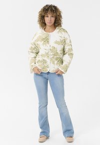 Veste matelassée en crème avec un motif floral vert, présentant un col rond, deux poches avant et un passepoil blanc le long des bords.