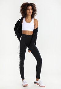 Sorte høye leggings med hvite side-striper med et mønster; parret med en hvit crop topp og en svart zip-up jakke.