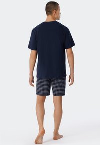 Navy blue cotton t-shirt with short sleeves, paired with checkered shorts featuring a white grid pattern on a dark background.