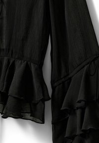 Black blouse featuring textured fabric with layered ruffle sleeves and a drawstring detail, accentuating soft, flowing lines.