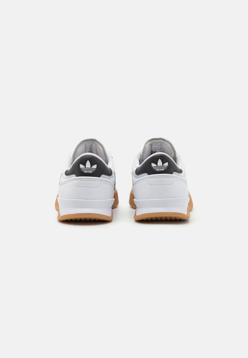 Weiße Sneaker mit einer Gummisohle, die eine schwarze strukturierte Fersenpartie und ein drei Streifen-Logo auf der Rückseite aufweisen. Aus glattem Leder.