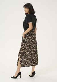 Zwarte t-shirt met korte mouwen, gecombineerd met een lange bruine patroonrok met een zijsplit, gedragen met zwarte stilettos.