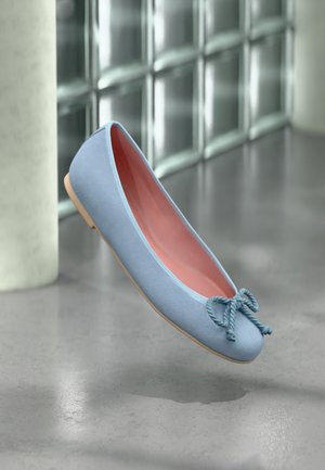 Hellblauer Ballerinaschuh mit einer Kordelschleife auf einem polierten Betonboden neben einer Glassteinwand und einer Säule.