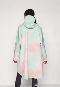 Lang regnjakke i pastell mintgrønn og rosa, med hette, lange ermer og et glatt, vannavvisende stoff.