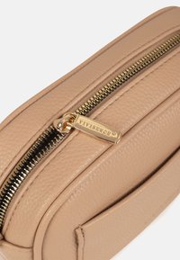 Primer plano de un bolso de cuero beige texturizado con tirador de cremallera dorado grabado con "VIVISENCE" en la parte superior.