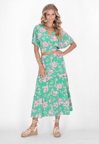 Completo floreale verde in due pezzi con top corto a maniche fluenti e gonna maxi a balze, decorato con fiori rosa e una vita elasticizzata.