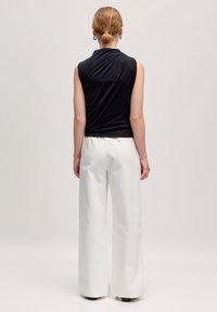 Zwarte mouwloze top van gladde stof, gecombineerd met losse witte broeken. De outfit heeft een ontspannen silhouet en minimale details.