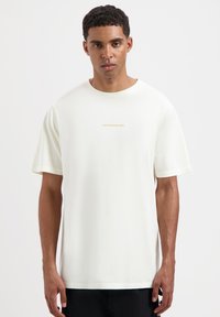 Witte katoenen t-shirt met korte mouwen en een ronde halslijn, met 'TOMORROWLAND' in gouden letters gedrukt in het midden.
