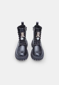Botas de cuero negro hasta el tobillo con suela gruesa, con cordones en la parte frontal y adornadas con acentos en forma de oso y de corazón.