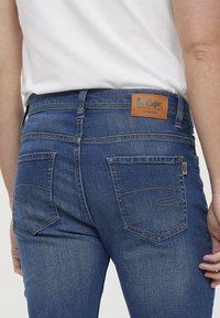 Donkerblauwe denim jeans met een middelhoge taille, twee achterzakken met een gekurveerde stitching en een tan lederen merkembleem op de tailleband.