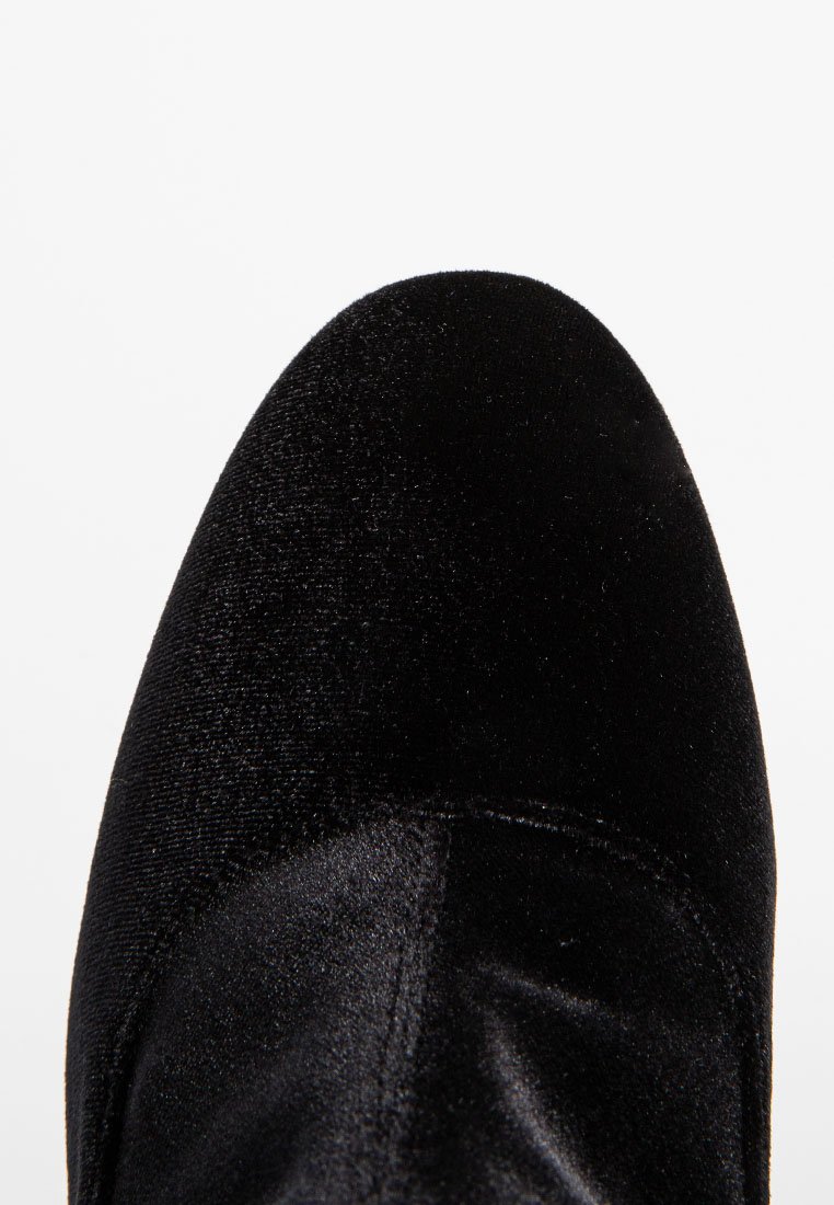 Nahaufnahme eines schwarzen Samt-Schuhzehens mit sichtbaren Nähten und weicher Textur vor einem schlichten weißen Hintergrund.