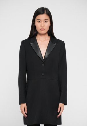 Abito blazer nero con rever in raso, chiusura con un solo bottone superiore e maniche lunghe, caratterizzato da una vestibilità sartoriale e una texture liscia.
