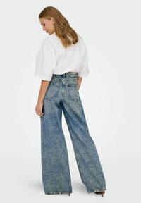 Hoge taille, wijde jeans in lichtblauwe denim met een vervaagde afwerking, voorzien van grote achterzakken en een rafelige zoom. Gecombineerd met een witte blouse.